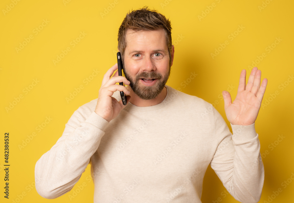 Young man in casual sweater talking on smartphone looking at camera with surprised face isolated over yellow background. Young man in casual sweater talking on smartphone looking at camera with surprised face isolated over yellow background.