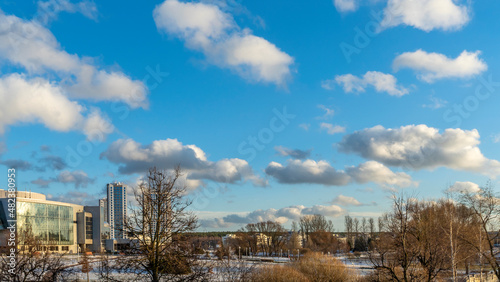A young city park against a bright blue sky with clouds. Urban landscape. First snow in the city.