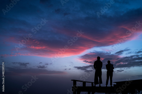 A couple is standing on the balcony looking at the colorful sky.