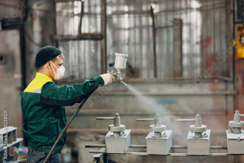 Powder primer coating of metal parts. Worker man in a protective suit sprays powder paint from gun on metal product construction at factory plant. photo