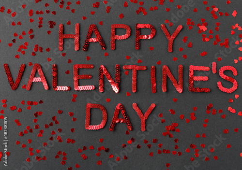 Inscription of "Happy Valentine's Day" embroidered with red sequins on black textured background with scattered random sequins in form of hearts