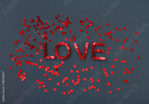 Inscription of "Love" embroidered with red sequins on black textured background with scattered random sequins in form of hearts