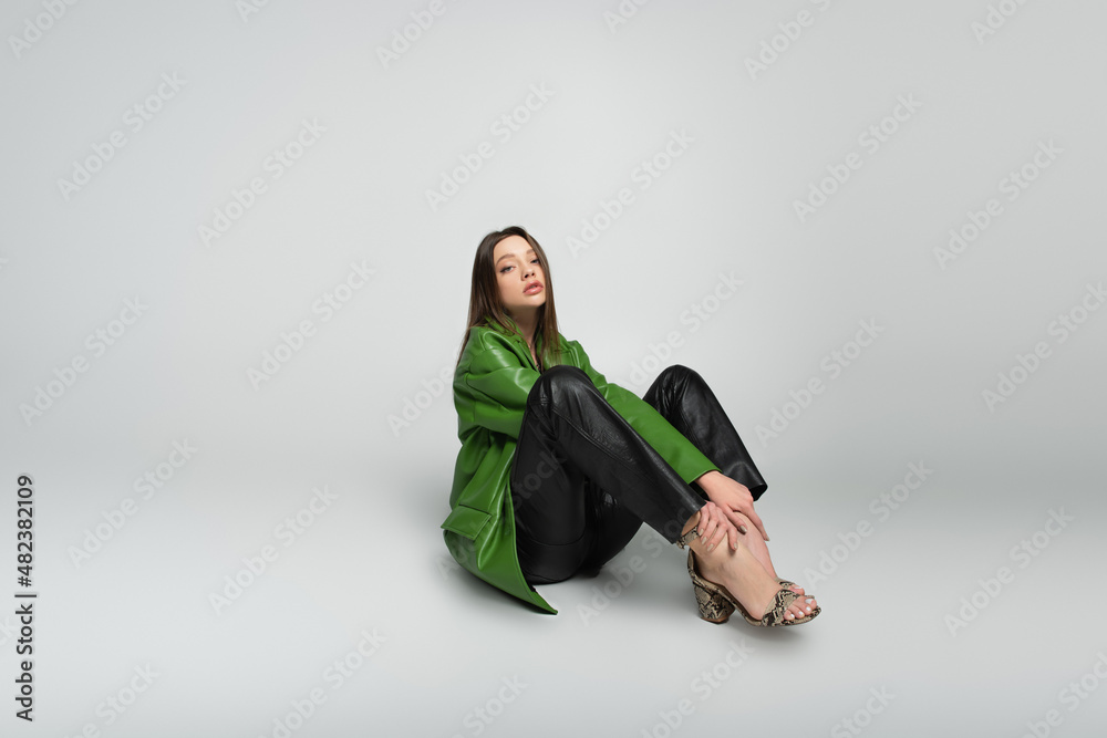 young woman in stylish leather jacket and trousers sitting on grey. young woman in stylish leather jacket and trousers sitting on grey.
