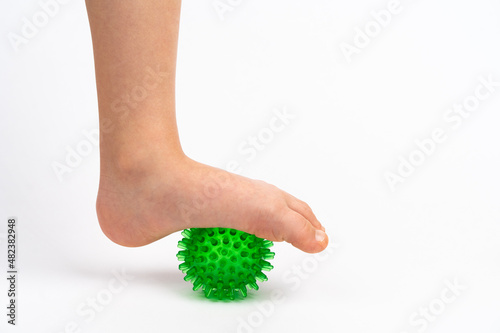 green needle ball for massage and physical therapy on a white background with a child's foot, the concept of prevention and treatment of foot valgus