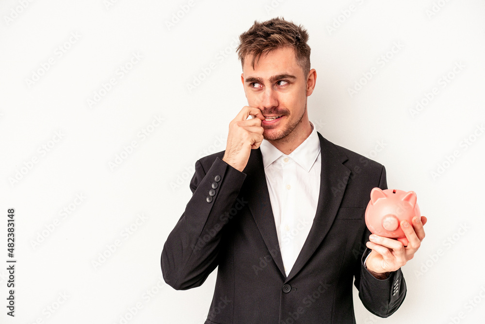 Young caucasian business man holding piggy bank isolated on white background relaxed thinking about something looking at a copy space. Young caucasian business man holding piggy bank isolated on white background relaxed thinking about something looking at a copy space.