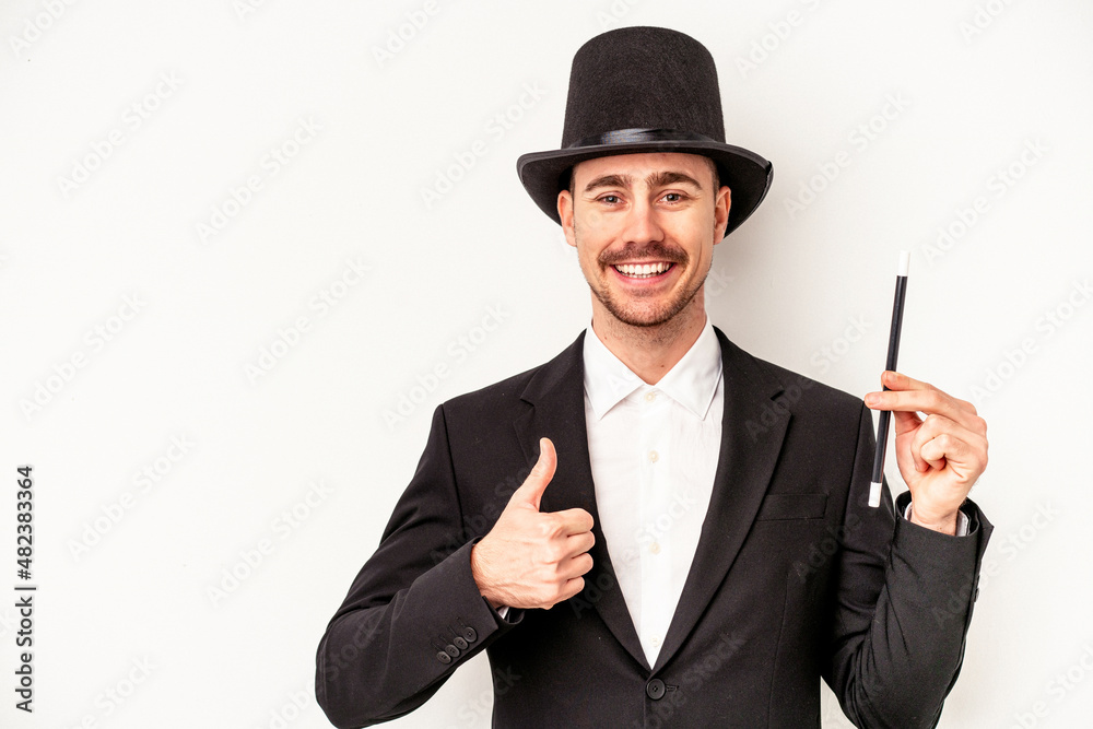 Young caucasian wizard man holding a wand isolated on white background smiling and raising thumb up Young caucasian wizard man holding a wand isolated on white background smiling and raising thumb up