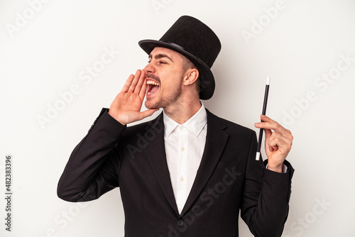 Young caucasian wizard man holding a wand isolated on white background shouting and holding palm near opened mouth.