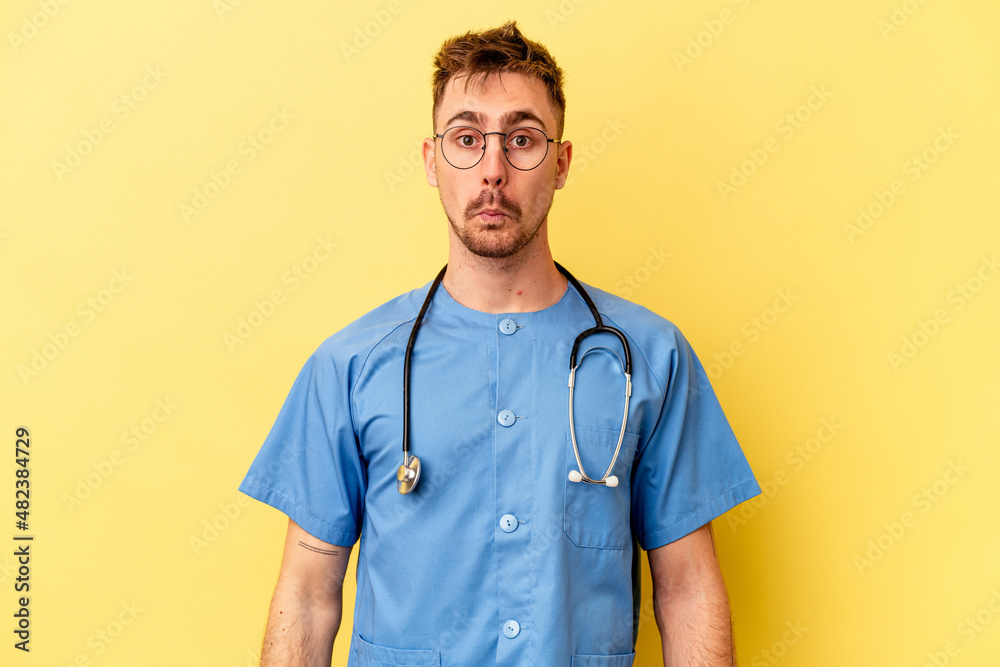Young nurse caucasian man isolated on yellow background shrugs shoulders and open eyes confused. Young nurse caucasian man isolated on yellow background shrugs shoulders and open eyes confused.
