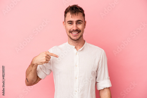 Young caucasian man isolated on pink background person pointing by hand to a shirt copy space, proud and confident photo