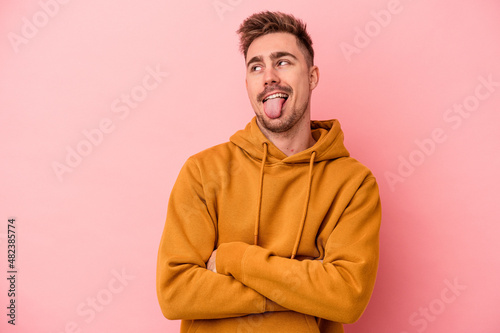 Young caucasian man isolated on pink background funny and friendly sticking out tongue.
