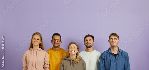 Group of happy joyful smiling young multiethnic Caucasian and mixed race Indian African people wearing hoodies and sweatshirts standing on purple background, looking up, thinking about something good
