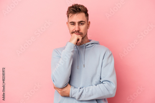 Young caucasian man isolated on pink background thinking and looking up, being reflective, contemplating, having a fantasy.