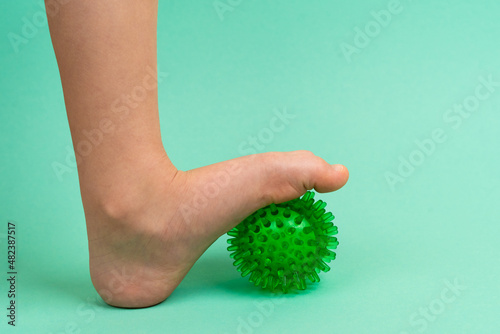 green needle ball for massage and physical therapy on a green background with a child's foot, the concept of prevention and treatment of foot valgus