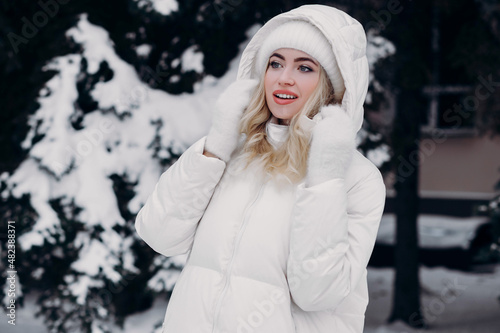 Beautiful European girl in a winter jacket against the backdrop of snowy pines.