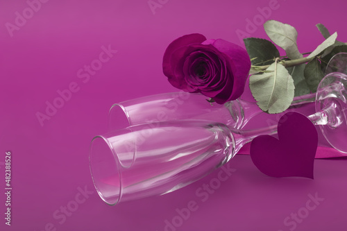 Two glasses and an elegant crimson rose on a crimson background.