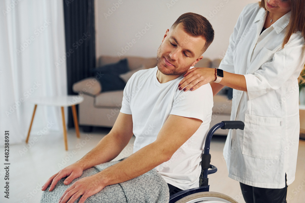 Fototapeta premium Woman is helping. Disabled man in wheelchair is at home