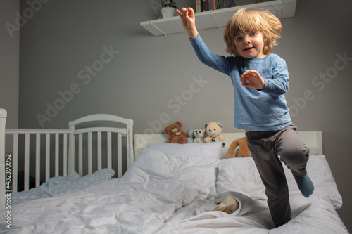 Child jumping on the parent's bed. Funny toddler. Playing baby. Baby in the motion. Happy childhood. Healthy baby moves and dances on the bed.