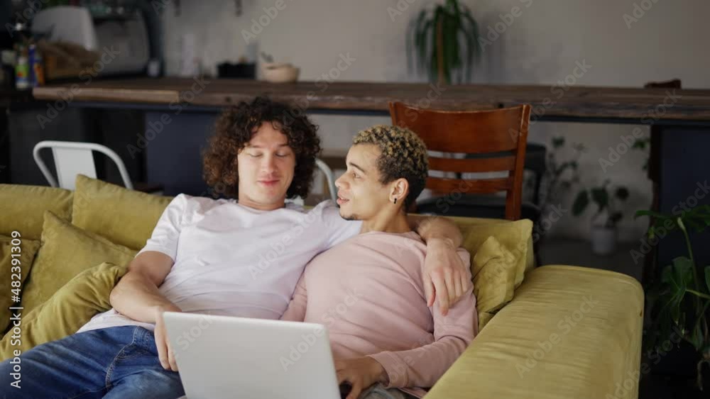 Handsome gay couple using laptop while sitting on a living room in cozy stylish apartment Handsome gay couple using laptop while sitting on a living room in cozy stylish apartment