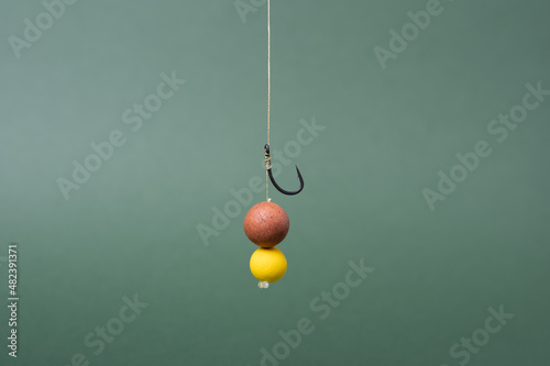 Carp fishing tackle concept, sharp fishing hook with boilie for carp fish. Yellow boilie on green backdrop. photo