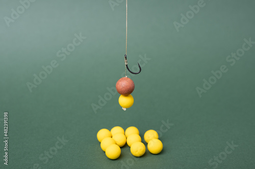 Carp fishing tackle concept, sharp fishing hook with boilie for carp fish. Yellow boilie on green backdrop. photo