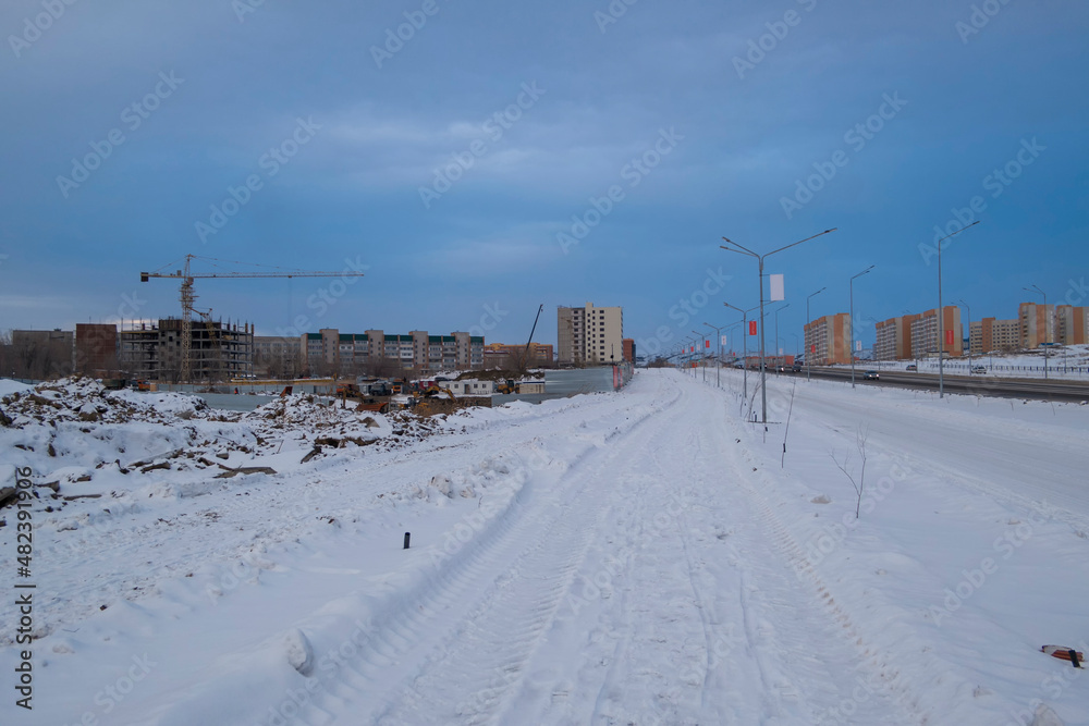 Newly built large avenue. New residential area. Construction site. Buildings under construction. White snow and blue sky. Ust-Kamenogorsk (kazakhstan)
