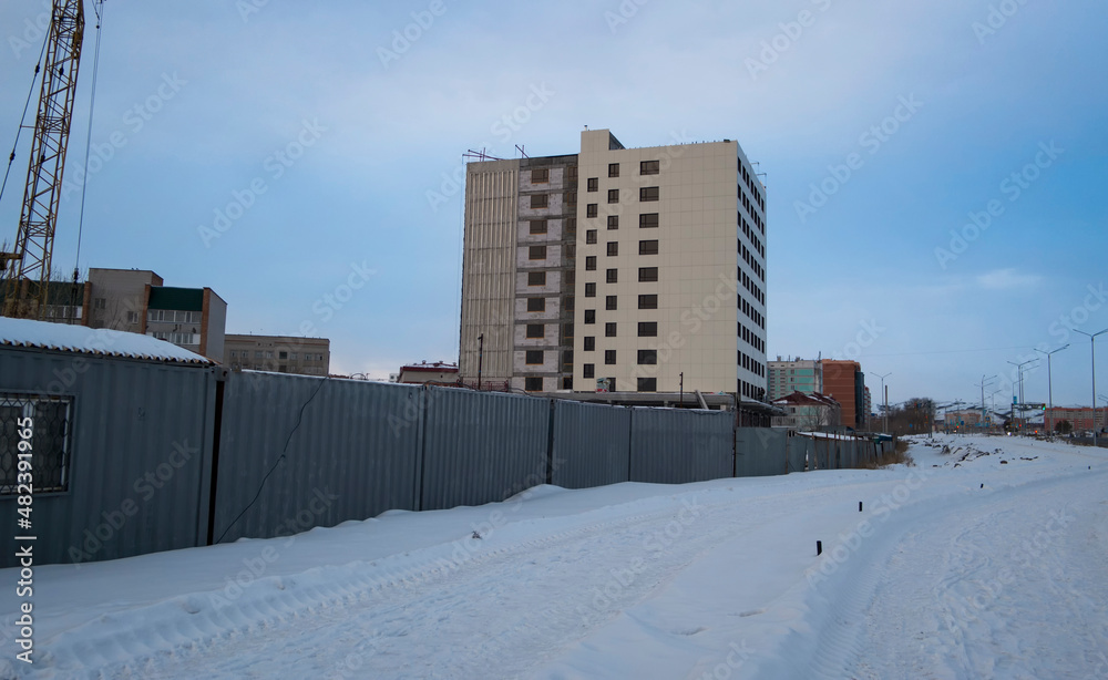 Newly built large avenue. New residential area. Construction site. Building under construction. White snow and blue sky. Apartment building. Ust-Kamenogorsk (kazakhstan)