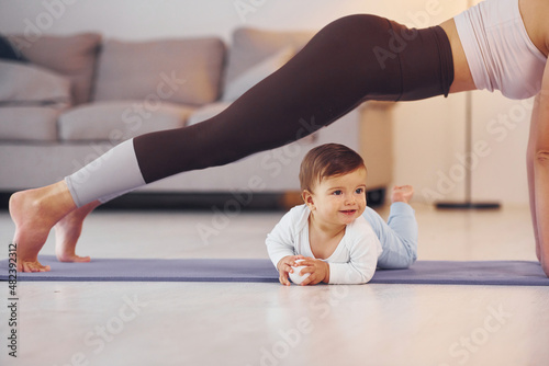 Woman doing exercises. Mother with her little daughter is at home together