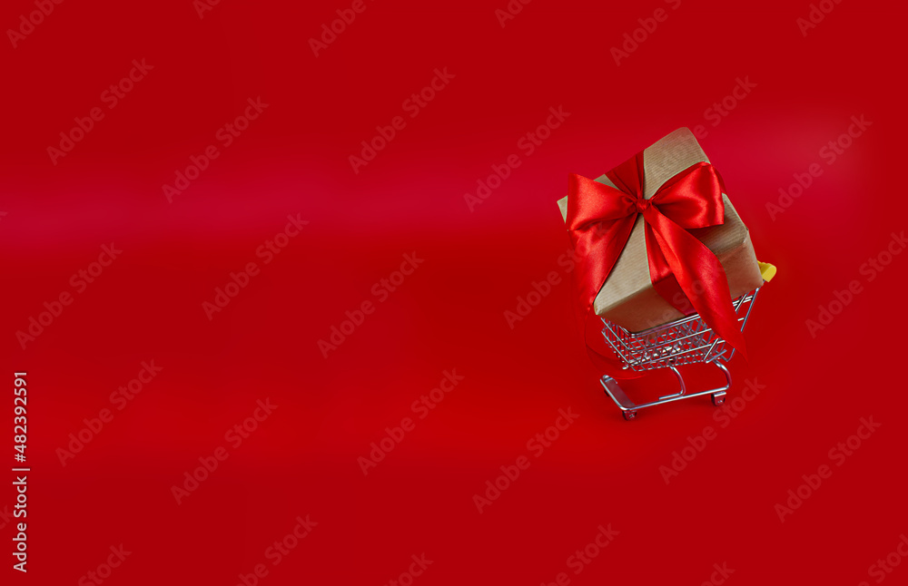 Gift with a red bow in a shopping cart on a red background. copy space. Festive background Gift with a red bow in a shopping cart on a red background. copy space. Festive background