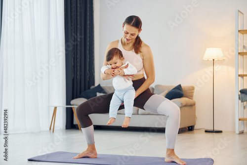 Standing on the mat and doing exerises. Mother with her little daughter is at home together