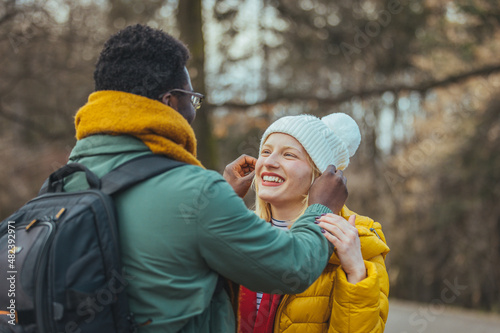 A cheerful couple in winter stands in front of each other outdoors. They both wear hats, jackets and scarves. They play on a cold day, spend time together.