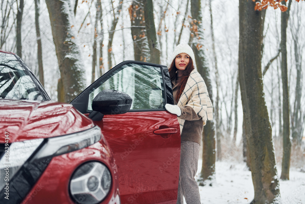 Positive emotions. Beautiful young woman is outdoors near her red automobile at winter time