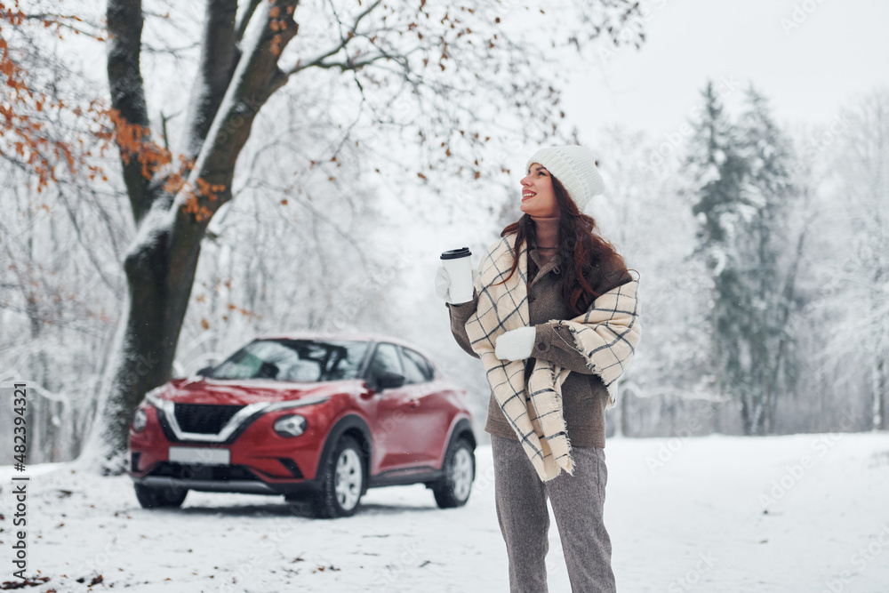 Non urban scene. Beautiful young woman is outdoors near her red automobile at winter time