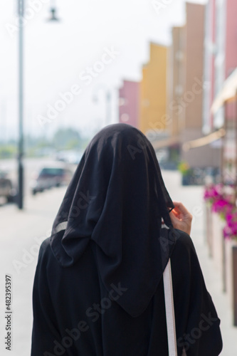 single Muslim woman walks through empty big city, rear view.