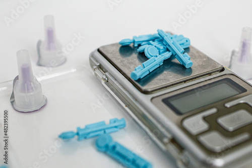 Blue lancets, needles with a spoon and scales on a white background