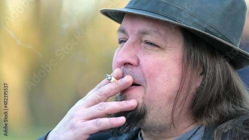[4k] close up of happy middle aged long haired rocker having a smoke outdoors
