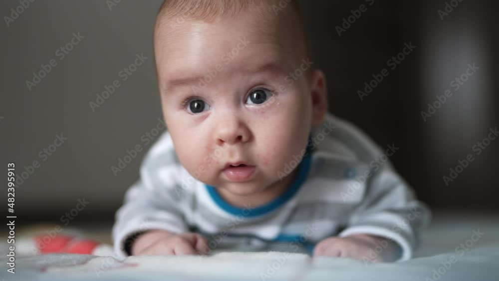 Interested look of a little toddler lying on his belly. Curious boy tries to keep his head and stares up. Close up. Interested look of a little toddler lying on his belly. Curious boy tries to keep his head and stares up. Close up.
