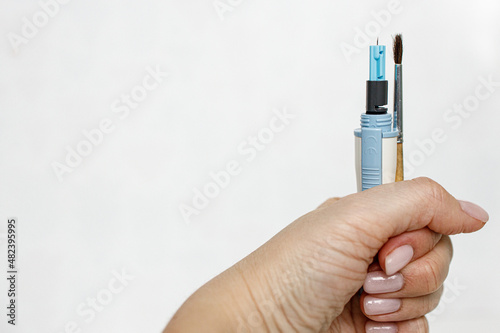 Female hand on a white background holds a lancet and an artistic brush
