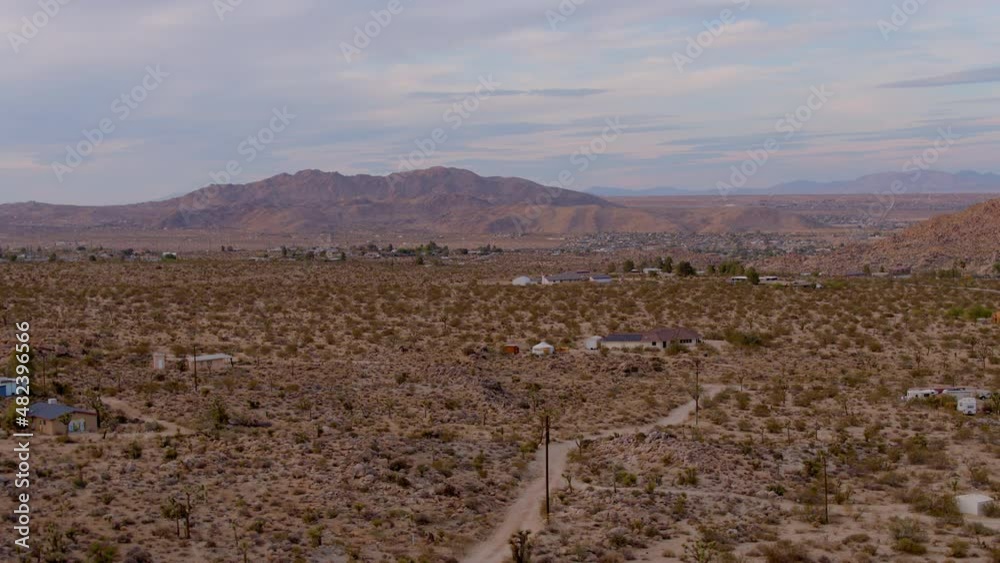 Boom up over dirt road and houses in desert of Joshua Tree, California with gorgeous mountains on horizon
