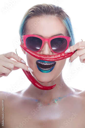 Portrait of Laughing Caucasian Girl Wearing Teeth Braces Having Fun With Red Pepper Against White.