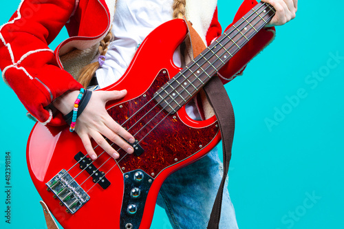 Music Ideas and Concepts. Closeup of Hands of Caucasian Guitar Player Posing With Bass Guitar In Fashionable Red Jacket Over Trendy Turquoise Background.