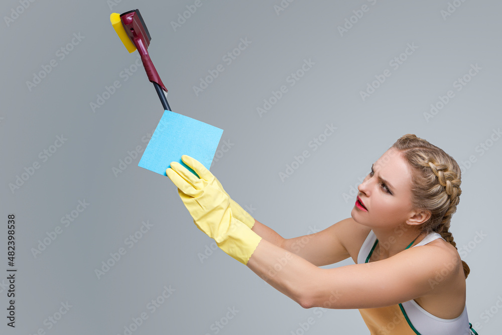 Household Working Caucasian Female Holding Blue Cleaning Sponge While Working In Yellow Rubber Gloves And Window Scraper. Household Working Caucasian Female Holding Blue Cleaning Sponge While Working In Yellow Rubber Gloves And Window Scraper.