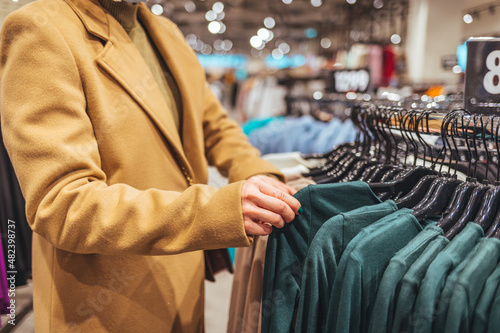 Female customer chooses clothes in a store, a blonde looks at a T-shirt in a boutique on a hanger, a woman buys on sale. The concept of shopping