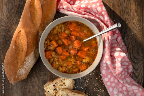 Bowl of chickpea soup with carrots, french bread baguette, red napkin, spoon and seed tectures photo