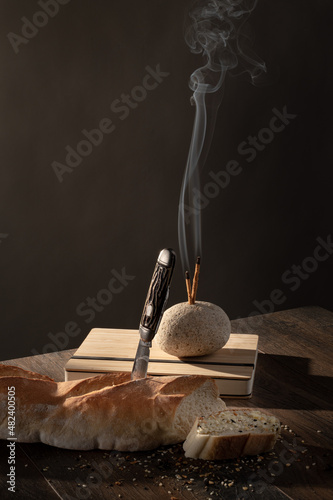 Still life with smokey incense,, bread, antique pocket knife, rocks and dark background on wood table top. photo
