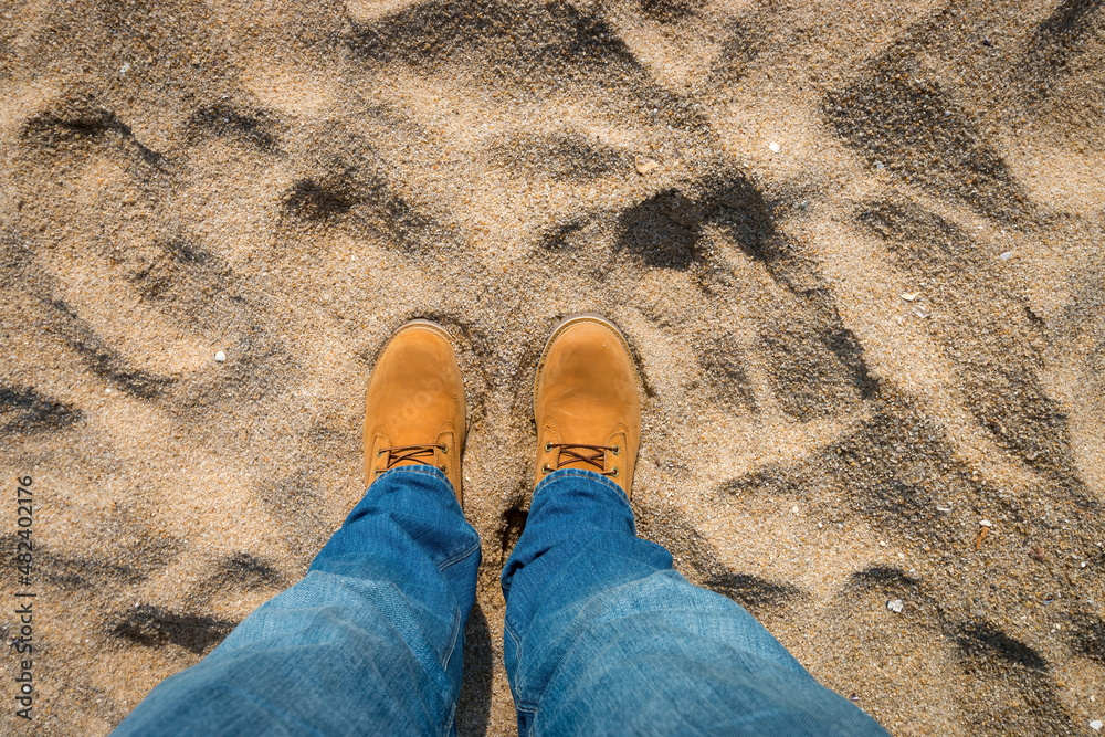 Fototapeta premium Legs and shoes of a person standing on sand.