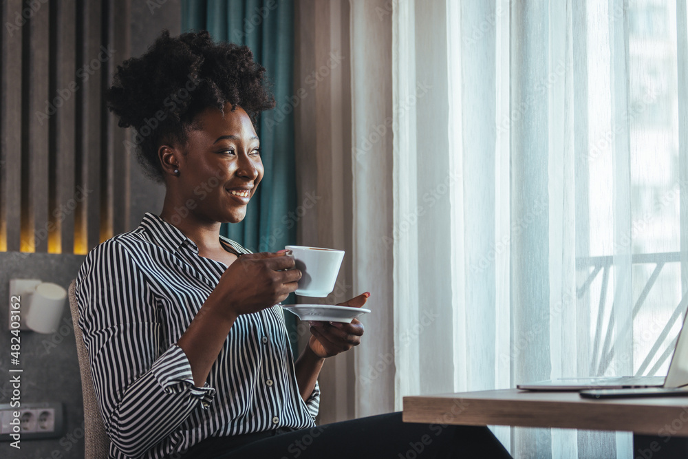 Close-up portrait of a smiling happy charming beautiful dreamer with black curly hair of a mature woman, drinking fresh morning coffee and sitting at a table in a hotel.