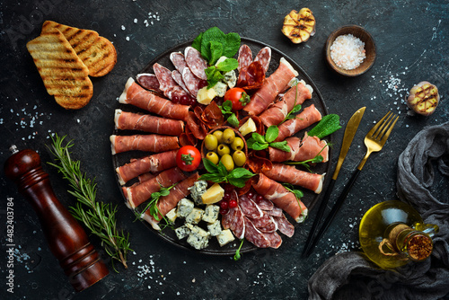 Italian prosciutto, dried pork, parmesan cheese, olives and snacks on a plate. Top view. On a gray stone background. photo