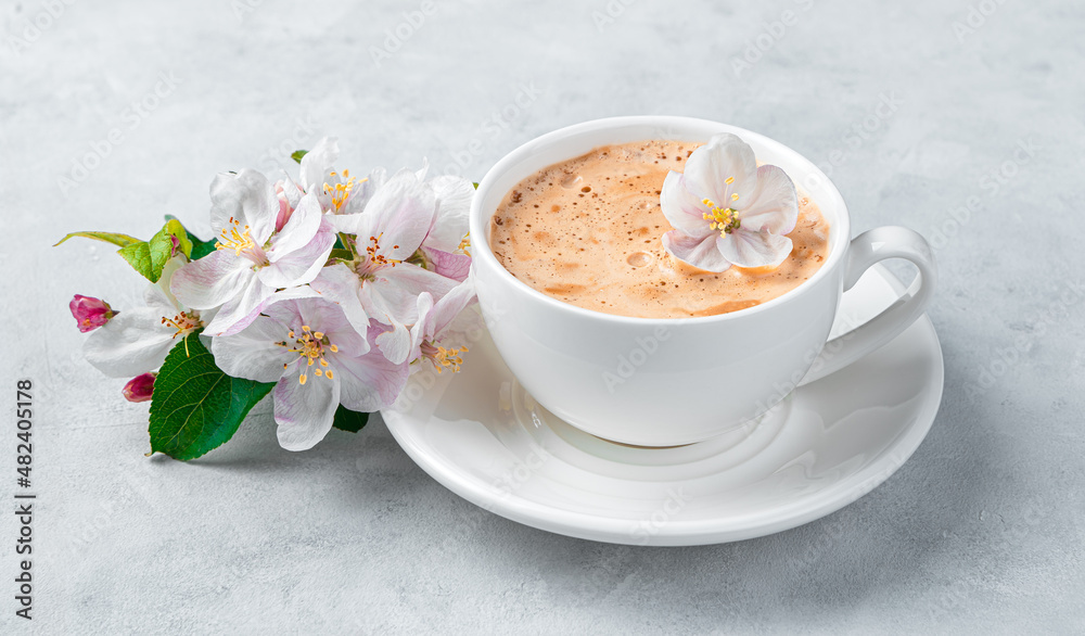 A cappuccino cup and a flowering branch on a gray background. A cappuccino cup and a flowering branch on a gray background.