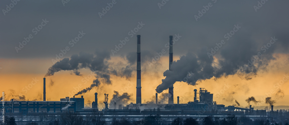 A panorama of a steel plant against the background of the orange sky. Smoking chimneys, environmental poisoning. Picture taken on a cloudy day, dramatic light.
