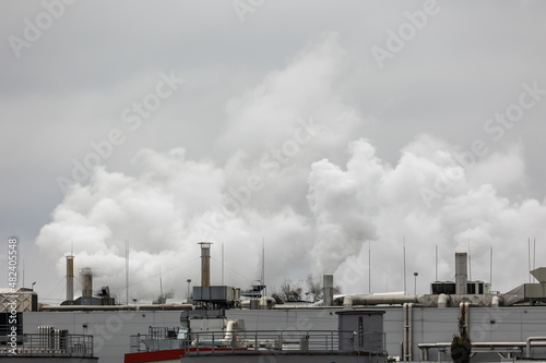 Puffs of steam coming out of chimneys on the roof of an industrial plant. Picture taken on a cloudy day, uniform and soft light.